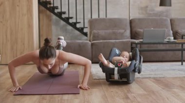 Sportif anne ve bacak protezi evde şınav çekerken bebek arabasının koltuğunda yatan oğluna bakıyor.