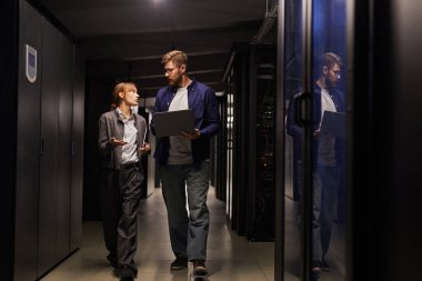 Farklı ağ aygıtlarıyla donatılmış bir sunucu odasında stratejiyi tartışan iki bilişim uzmanı. Bir teknisyen dizüstü bilgisayar tutuyor, diğeri el hareketleriyle bir şey anlatıyor.