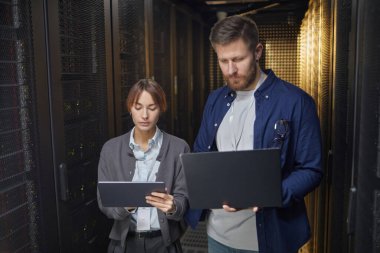Bir veri merkezinde birlikte çalışan iki bilişim uzmanı, sunucuları ve ağ ekipmanlarını izlemek için tablet kullanarak verimli ve organize bir ortam yaratıyorlar.
