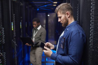 Modern bir veri merkezi sunucu odasında çalışan mühendisler, aygıtları kontrol ediyor ve sunucu raflarını koruyor, ideal performansı sağlıyor. Profesyonel ve güvenli bir ortamda işbirliği yapan teknisyenler