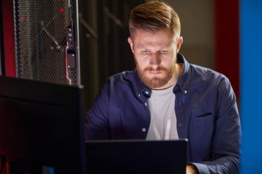 Ofisteki bilgisayarı yakından inceleyen beyaz bir adamın portresi. Ciddi ifade, sakal ve günlük iş kıyafetleriyle donatılmış.