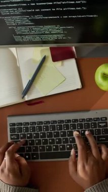 Ofis masasında açık bir telif defteri, bir fincan kahve ve elma ile çalışan tanınmayan bir programcının el açısıyla çekilmiş yüksek açılı görüntüsü.