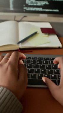 Bilgisayarda program kodu ve bilgisayar ofis masasında otururken tanımlanamayan yazılım mühendisinin dikey POV görüntüsü