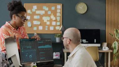 Orta yaşlı beyaz erkek programcının çalışmalarını kontrol eden kendinden emin genç Afrikalı Amerikalı kadın patronun modern ofisteki bilgisayar masasında oturan yeni yazılımını gösteren orta boy fotoğrafı.