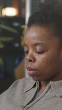 Modern ofis masasında çalışan odaklanmış genç Afro-Amerikan yazılım geliştiricisinin dikey yakın çekimi. Program kodları ekranda bulanık arka planda çalışıyor.