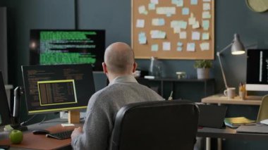 Gözlüklü orta yaşlı beyaz erkek programcı. Gündüz vakti modern ofiste Afrikalı Amerikalı kadın meslektaşımla çalışırken bilgisayara program kodları yazıyor.