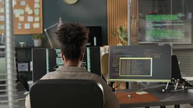 Programlama kodlarıyla çalışan odaklanmış genç Afrikalı Amerikalı kadın programcının bilgisayar önünde ve boş bilişim bürosundaki bilgisayar başında oturması.