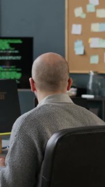 Orta yaşlı, gözlüklü beyaz erkek programcının dikey hâli. Bilgisayarda program kodlaması ile çalışırken Afrika kökenli Amerikalı bir bayan meslektaşın modern ofise girmesi.