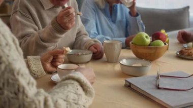 Huzurevinde huzur içinde yemek yiyorlar. Bir adam mısır gevreği yerken diğerleri çay yudumluyor ve gülümsüyor. Etrafı meyve ve sıcak sohbetlerle çevrili.