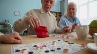 Yasli arkadaslarinin yakinlarinda tombala oynarlarken, masada otururken, yanlarinda abur cuburlar ve sicak içeceklerle sıcak huzurevinde