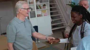 Orta boy gülümseyen beyaz bir adam huzurevinde genç siyahi kadın bakıcı ile dans ediyor, hepsi de gündüz eğleniyor.