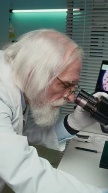 Mikroskoba bakan Kafkas erkek bilim adamının dikey yavaş çekimi. Sonra laptop ekranında dijital büyütülmüş görüntüyü analiz ederek modern, iyi donanımlı bir laboratuarda çalışıyor.