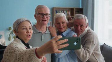 Yaşlı, beyaz bir adam, neşe dolu ve neşeli bir anı yakalamak için huzurevindeki ev arkadaşlarıyla eğlenceli grup selfie 'sine katılmak için gülümsüyor.