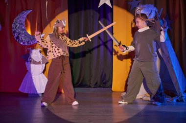 İki çocuğun seyirci koltuğundan uzun bir çekim. Sahne ışıkları altında savaşan iki şövalye çocuk tiyatrosunda oynuyor.