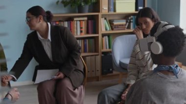 Genç grup terapi seansı sırasında VR kulaklıklı Z genini destekleyen empatik genç çift ırklı kadın danışmanın yavaş çekimleri.