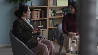 Yakın danışmanlık bürosundaki terapi sırasında Asyalı gen Z kadın hastasıyla konuşma yapan melez genç kadın psikologların orta ölçekli bir fotoğrafı.