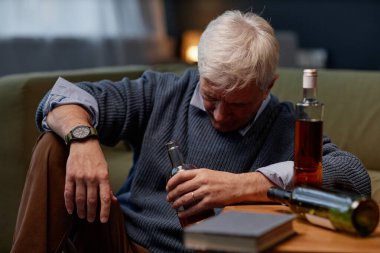 Diğer şişeler ve kitap hediye edilirken kıdemli adam masada oturup şişeyi inceliyor. Konforlu bir ev ortamında oturmuş düşünceli görünüyor.