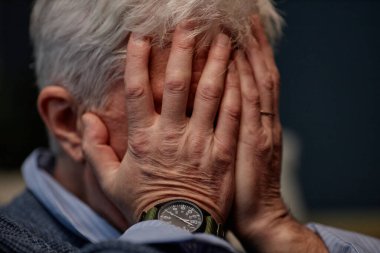 Yaşlı bir birey el ele tutuşuyor, kol saatini gösteriyor ve süveter giyiyor, düşünce ve mahremiyet ortamı yaratıyor.