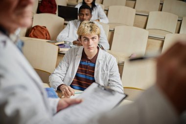 Üniversitede ön planda tanınmayan bir profesörle konferans dinlerken genç bir adamın portresi.