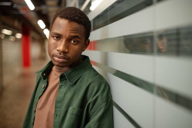 Okul çıkışında cam duvara yaslanan Afrikalı Amerikalı bir gencin yan görünümü.