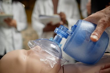 Kolej konferans salonunda not alan bir grup öğrenciye suni teneffüs tekniği gösteren kıdemli tıp profesörünün yan görüntüsü.