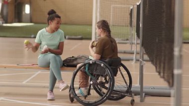 Eğitimden sonra tekerlekli sandalyedeki kadın sporcuyla konuşan ve meyve yiyen çok kültürlü genç bir kadın.