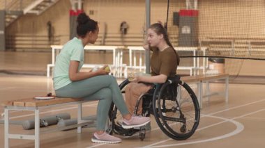 Uzun zamandır tekerlekli sandalyede kıvırcık saçlı kız arkadaşıyla spor salonunda konuşuyor ve meyve yiyor.