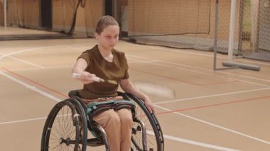 Spor salonunda antrenmandan önce orta boylu, tekerlekli sandalyedeki kız öğrencinin badminton raketiyle ısınması.