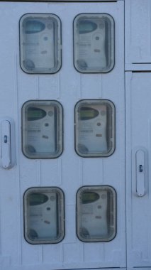 Enerji kullanım verilerini gösteren şeffaf kapaklar içeren beyaz bir duvara konut ortamlarında modern teknolojiyi vurgulayan altı kullanım ölçer yerleştirilmiştir.