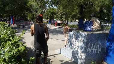 People skateboarding and relaxing at an outdoor skatepark on a sunny summer day.