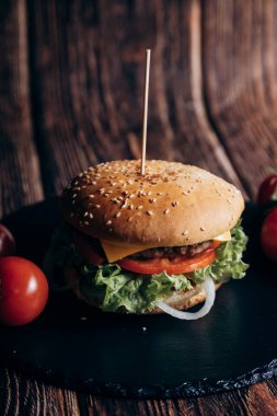 Fresh tasty grilled burger with meat, tomato and lettuce lie on plate. Meat cutlet, tomatoes, cucumber, lettuce and sesame seeds. Fast food concept. junk food