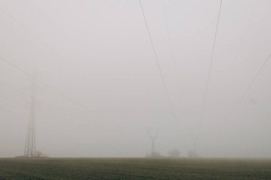 Power lines in the middle of field with fog during day. energy crisis