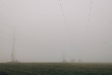 Power lines in the middle of field with fog during day. energy crisis