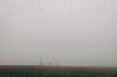 Power lines in the middle of field with fog during day. energy crisis