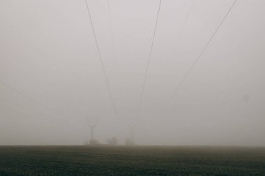 Power lines in the middle of field with fog during day. energy crisis
