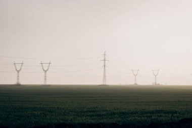 Power lines in the middle of field with fog during day. energy crisis