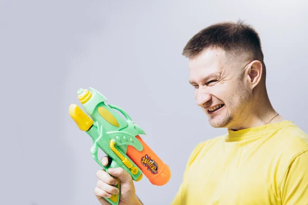 Man in yellow T-shirt holds water pistol in his hand. Attractive guy