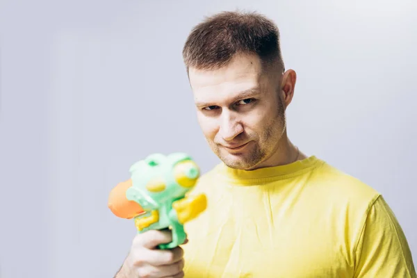 Man in yellow T-shirt holds water pistol in his hand. Attractive guy
