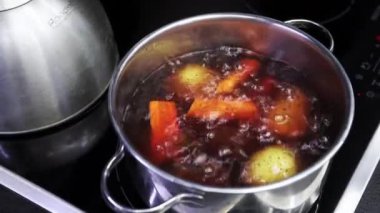 Water boils in steel pot and vegetables are boiled for salad