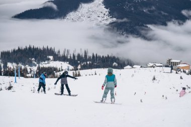 Snowboarder in jacket stands on top of mountain and posing to camera