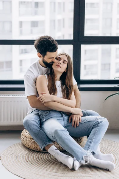 Young cute couple in white t-shirts and blue jeans stand in new apartment and rejoice in happiness