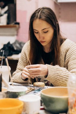 Kız aletlerin yardımıyla kilden heykel yapıyor. Çiğ kille çalışmak. Özel bir aracın yardımıyla, atölyedeki kadın ana çömlekçi masası fazlalığı kaldırır