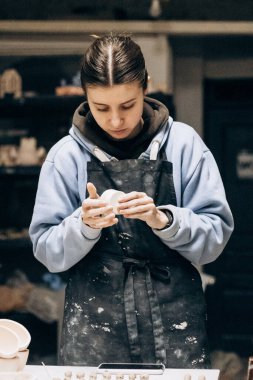 Kız aletlerin yardımıyla kilden heykel yapıyor. Çiğ kille çalışmak. Özel bir aracın yardımıyla, atölyedeki kadın ana çömlekçi masası fazlalığı kaldırır