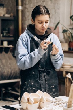 Kız aletlerin yardımıyla kilden heykel yapıyor. Çiğ kille çalışmak. Özel bir aracın yardımıyla, atölyedeki kadın ana çömlekçi masası fazlalığı kaldırır