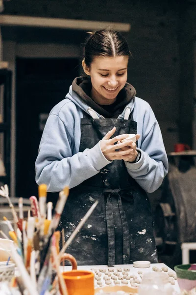 Girl sculpts from clay with the help of tools. Working with raw clay. Female master potter table in workshop With the help of a special tool, removes excess