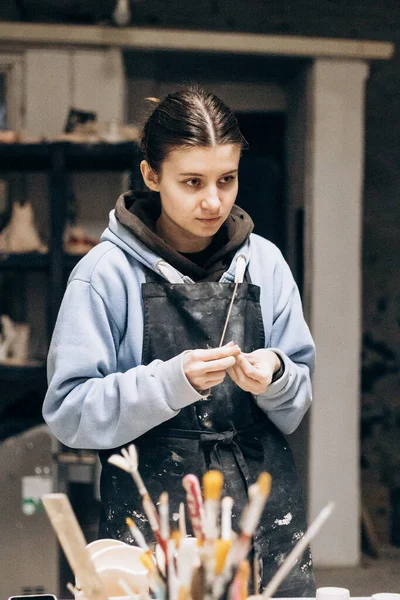 Girl sculpts from clay with the help of tools. Working with raw clay. Female master potter table in workshop With the help of a special tool, removes excess