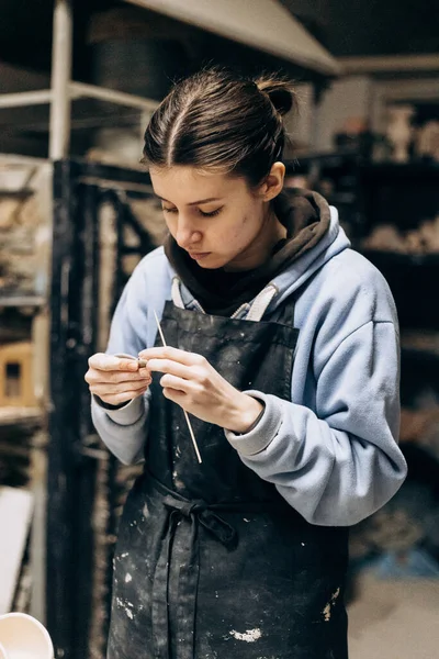 Girl sculpts from clay with the help of tools. Working with raw clay. Female master potter table in workshop With the help of a special tool, removes excess