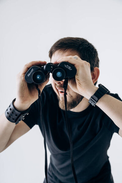 Парень в черной футболке держит бинокль и смотрит в него