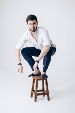 Beyaz gömlekli, sakallı yakışıklı bir adam portresi sandalyede oturuyor.