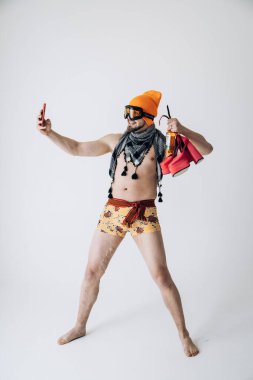 Şapkalı ve kayak gözlüklü bir adam ellerinde sarı lastik eldivenler ve pembe kadın ayakkabıları ile selfie çekiyor. 